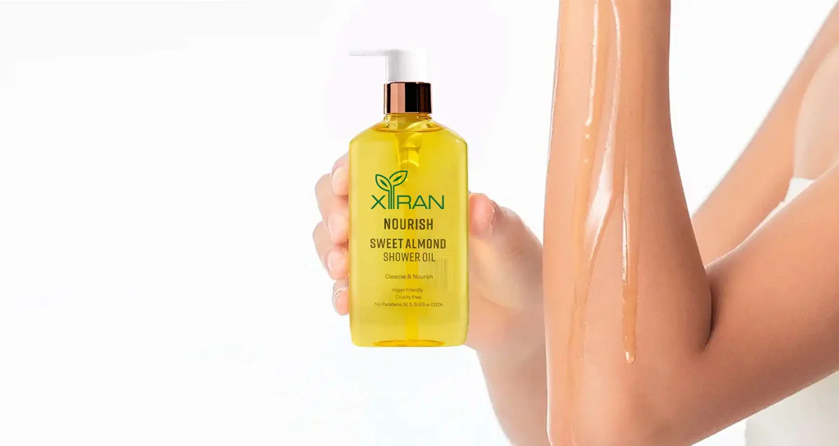 Bottle of Xiran Sweet Almond Shower Oil held next to an arm with oil applied, showcasing product and skin nourishment.